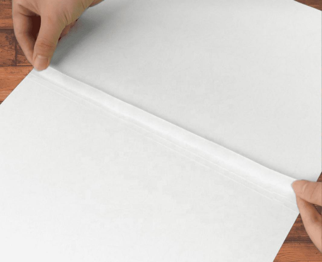 Hands folding white paper on table.